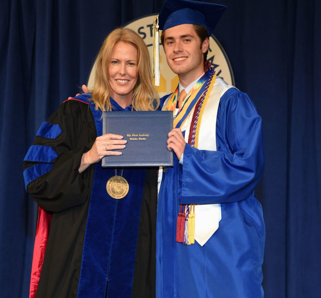 A high school graduate in cap and gown standing next to a woman