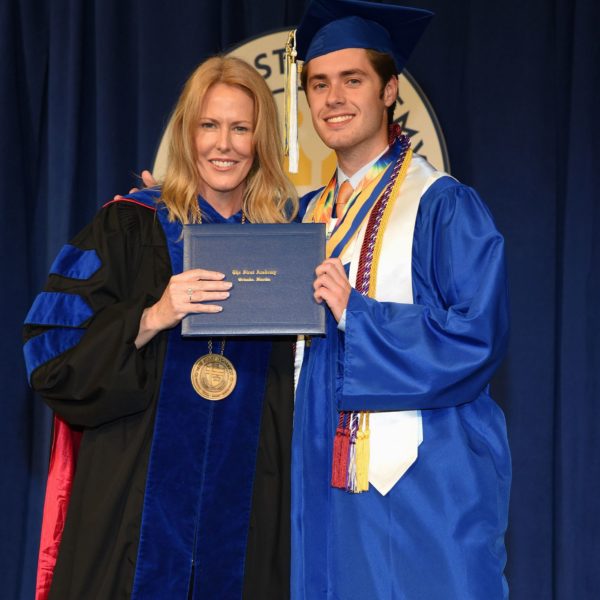 A high school graduate in cap and gown standing next to a woman