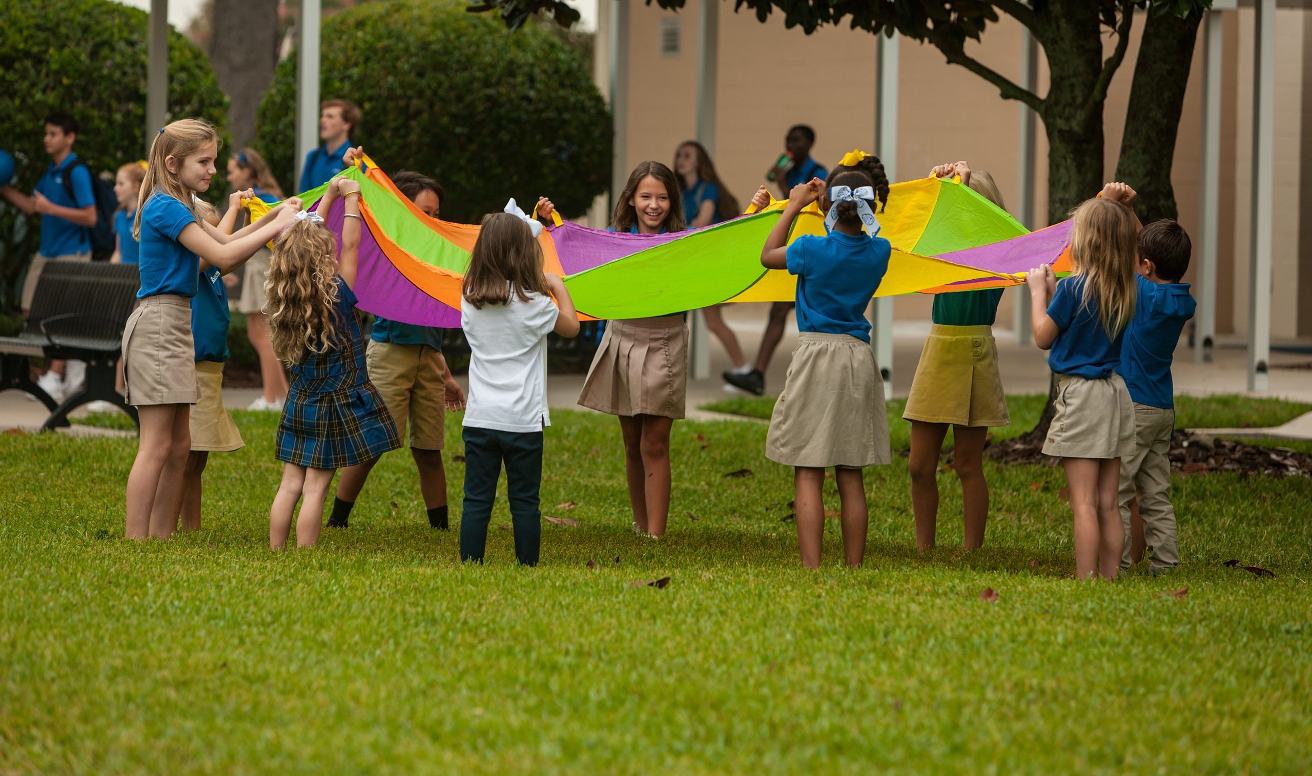 Several young children in a playground holding up a multi-colored parachute