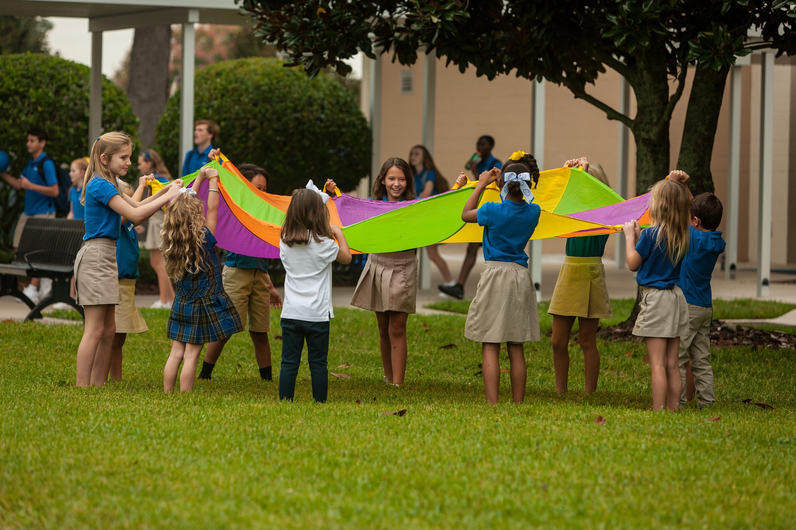 Several young children in a playground holding up a multi-colored parachute